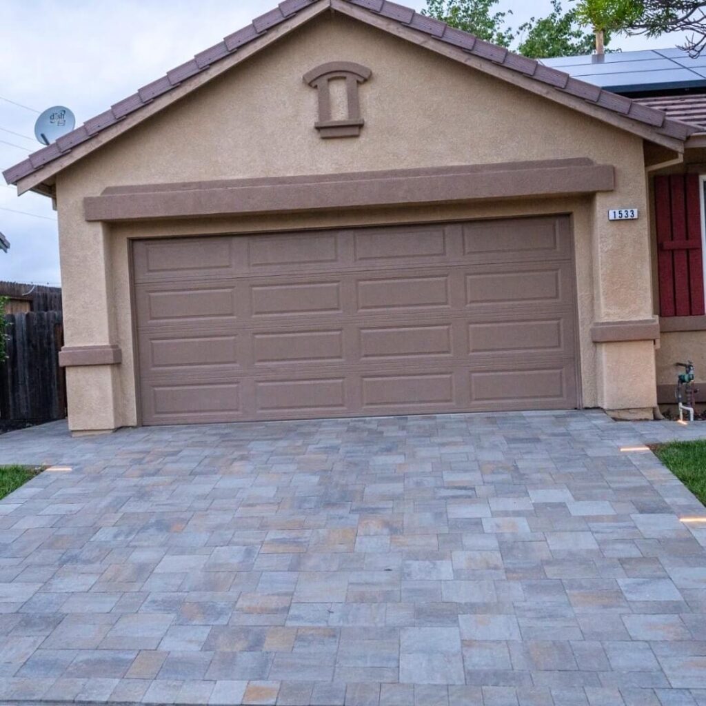 Front facade of a beige suburban home, featuring a brown garage door, tiled driveway in muted tones, and address number 1533. A satellite dish and residential surroundings complete the scene.