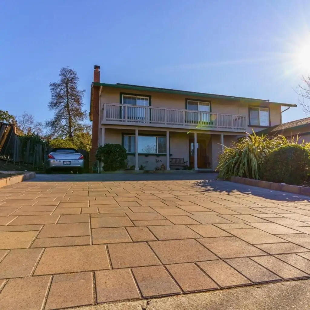Two-story green suburban home with spacious balcony, paved driveway, parked sedan, and lush landscaping, illuminated by the setting sun. Perfect for real estate and property showcases.