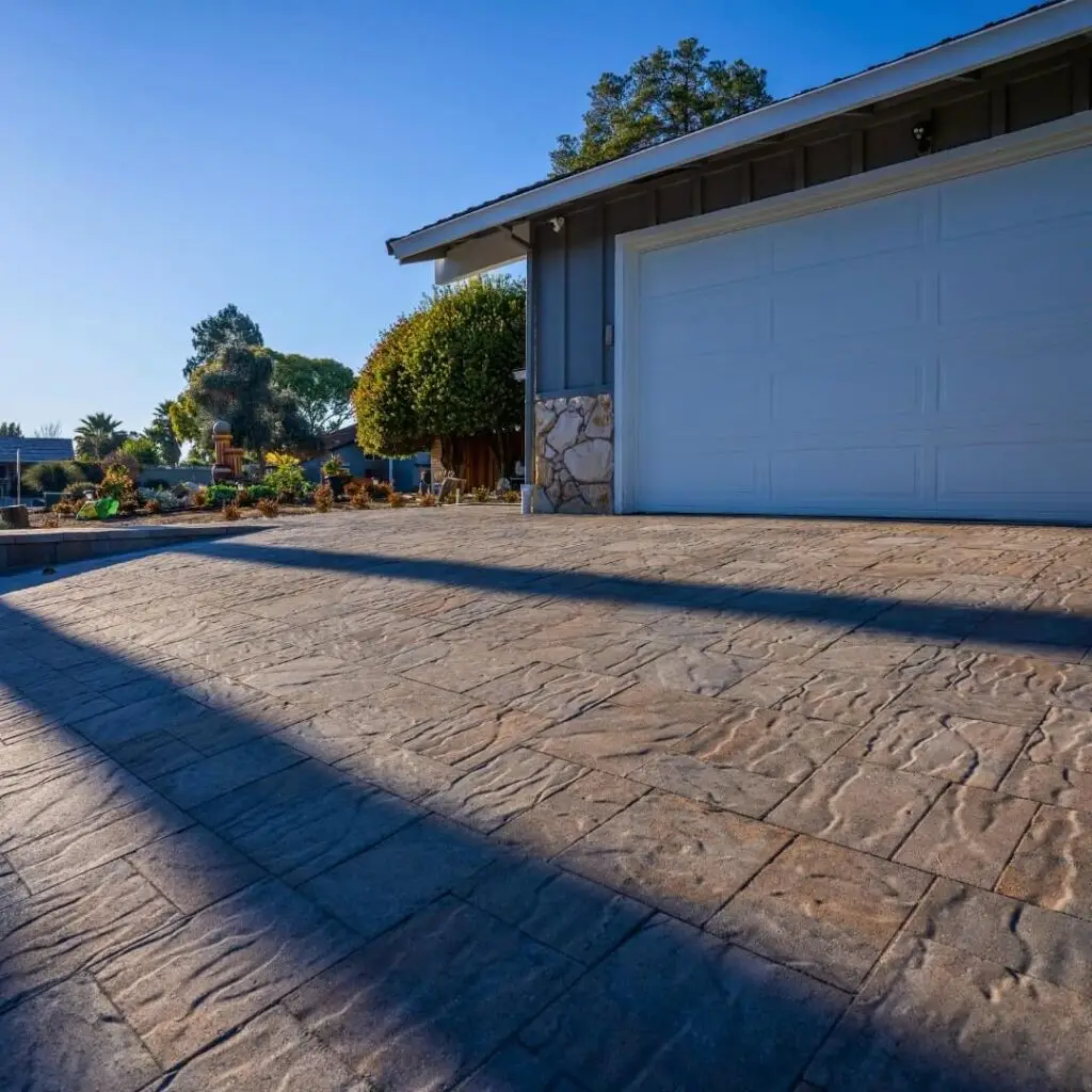 Modern home exterior featuring a spacious stamped-concrete paver driveway, white garage door, and well-manicured garden with vibrant plants, ideal for residential real estate listings.