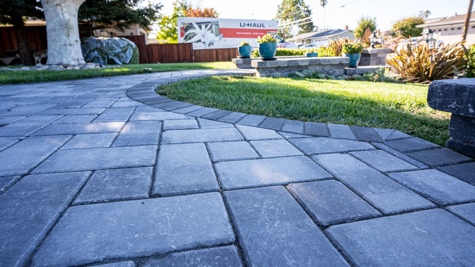 Curved stone paver pathway in a landscaped yard with a U-Haul truck in the background.